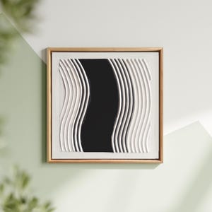 Puede incluir: Cuadro enmarcado cuadrado con marco dorado. La obra presenta una franja vertical negra en el centro, flanqueada por líneas verticales blancas y onduladas. La pieza está montada sobre un fondo blanco.