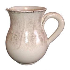 Puede incluir: Jarra de cerámica color crema con cuerpo redondeado y asa curva. La jarra tiene un borde ligeramente ensanchado y un acabado texturizado y envejecido con detalles grises. Un artículo de menaje decorativo.