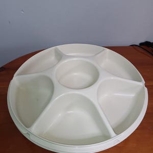 Op de afbeelding: Een witte, ronde serveerschaal met zes compartimenten en een centrale put. De schaal is gemaakt van een glad, duurzaam materiaal en is ontworpen voor het serveren van snacks, hapjes of dips. Ideaal voor feesten en bijeenkomsten.