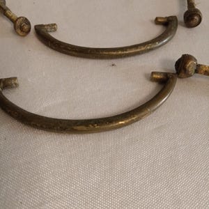 May include: A collection of semi-circular brass drawer pulls featuring a weathered, aged finish. Each handle is curved with two mounting posts at the ends, accompanied by threaded metal bolts and circular nuts for secure attachment to furniture.