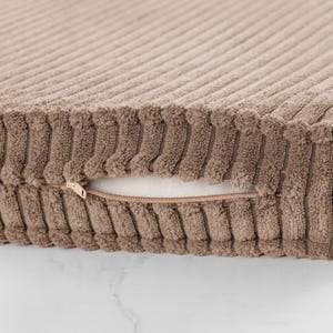 A close-up view of a brown, textured fabric with a zipper pull visible.