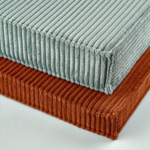 Peut inclure: Deux coussins de sol rectangulaires empilés l'un sur l'autre. Le coussin supérieur est de couleur vert sauge clair et le coussin inférieur est de couleur orange brûlé. Les deux coussins présentent une texture en velours côtelé vertical.
