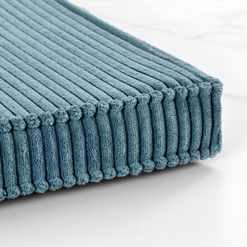 A close-up view of a textured, blue-green fabric with a ribbed or striped pattern, resting on a white surface.