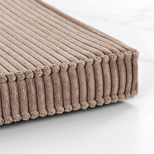 A close-up view of a textured, beige-colored fabric, possibly a cushion or textile, resting on a white surface.