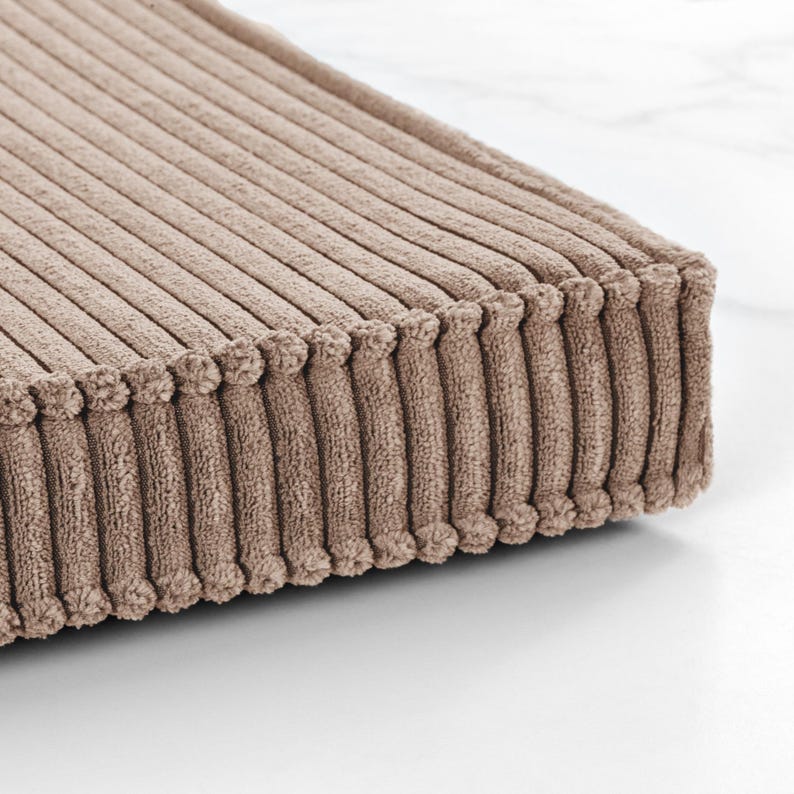 A close-up view of a textured, beige-colored fabric, possibly a cushion or textile, resting on a white surface.