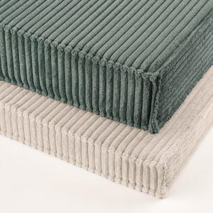 two rectangular cushions, one green and one beige, stacked on top of each other.