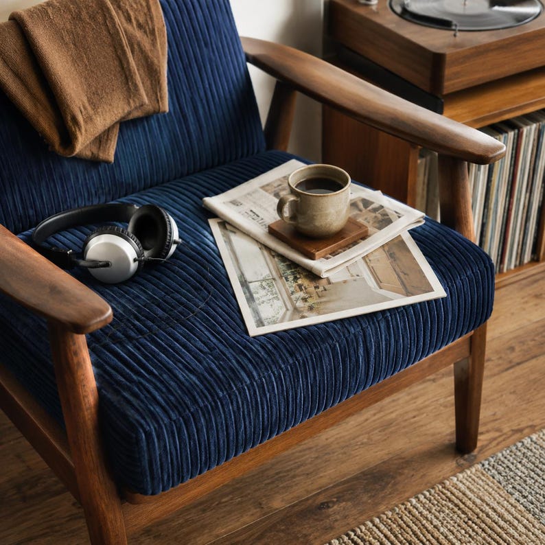 A cozy armchair with a pair of headphones, a newspaper, and a cup of coffee on its seat, set against a wooden floor and a bookshelf in the background.