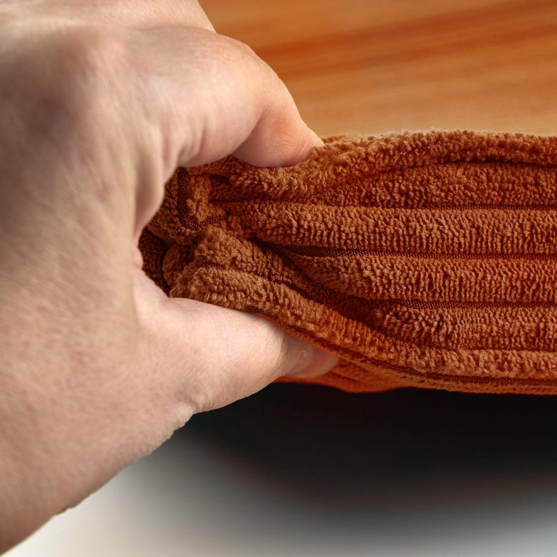 A hand is holding a folded orange towel, with the towel's texture and folds visible.