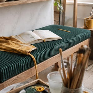a cozy and creative workspace with a wooden bench, an open book, and various art supplies such as paintbrushes and a cup.