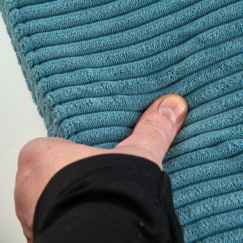 A close-up image of a person's hand holding a blue, textured fabric, with the thumb pointing towards the fabric.