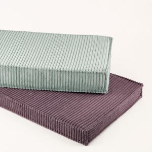 two rectangular cushions, one light green and one dark purple, placed on top of each other against a white background.