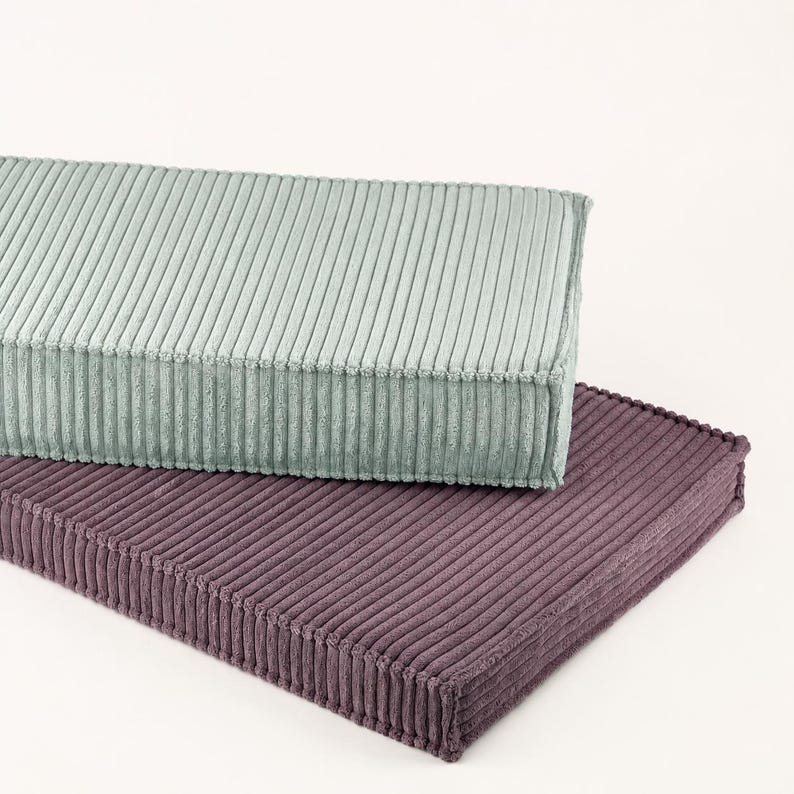two rectangular cushions, one light green and one dark purple, placed on top of each other against a white background.