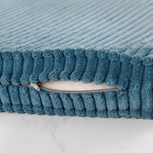 A close-up view of a blue, textured fabric with a zipper pull visible.
