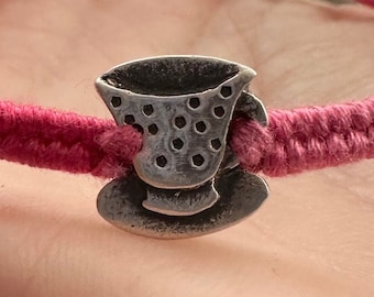 A sweet little handmade fine silver tea cup on a vivid pink leather, cotton and sterling silver friendship bracelet.