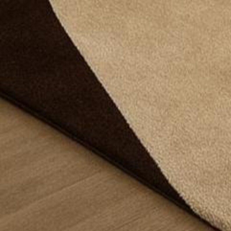 May include: A close-up of a brown and tan rug with a soft, textured surface. The rug is divided diagonally, with a dark brown section and a lighter tan section. The rug is on a light brown wooden floor.