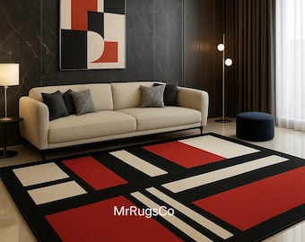 May include: A modern area rug with a geometric design featuring red, black, and white rectangular shapes. The rug has a black border and is placed in a living room setting with a sofa, artwork, and a lamp. The text "MrRugsCo" is visible on the rug.