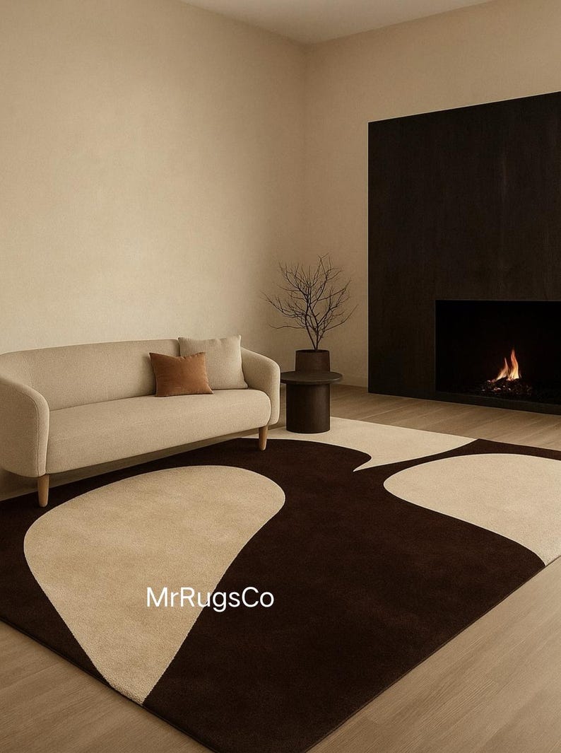 May include: A modern living room featuring a beige sofa with brown accent pillows, a dark brown rug with a beige abstract design, and a fireplace. A small side table holds a decorative plant. The room has a neutral color palette.