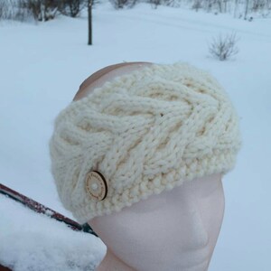 May include: White knitted headband with a cable knit pattern and a wooden button with the text "Simply Handmade" on it.