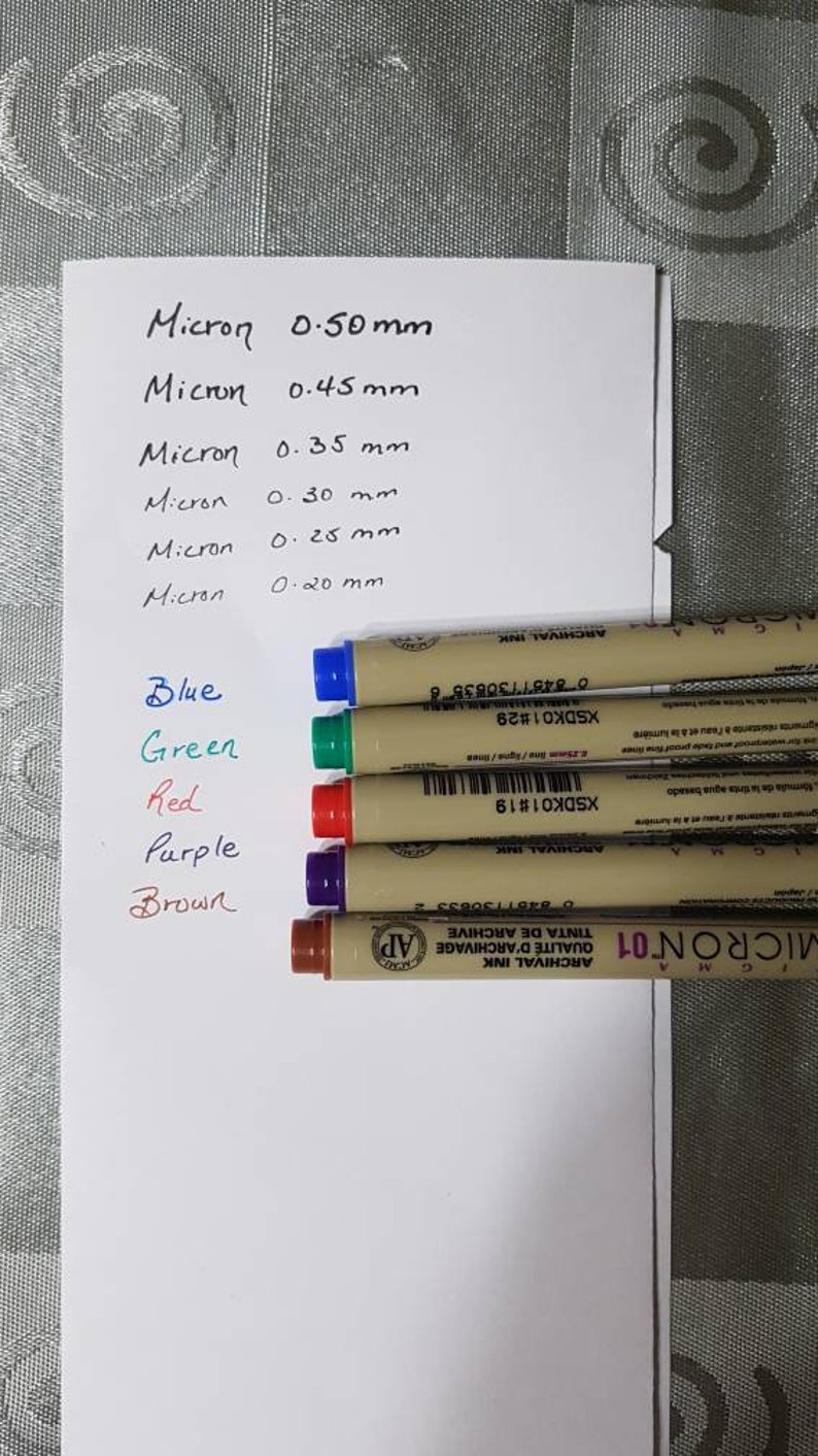 Puede incluir: Cinco bol&iacute;grafos de tinta de archivo de la marca Micron en azul, verde, rojo, morado y marr&oacute;n. Los bol&iacute;grafos est&aacute;n etiquetados con el tama&ntilde;o de la punta en mil&iacute;metros: 0,50 mm, 0,45 mm, 0,35 mm, 0,30 mm, 0,25 mm y 0,20 mm.
