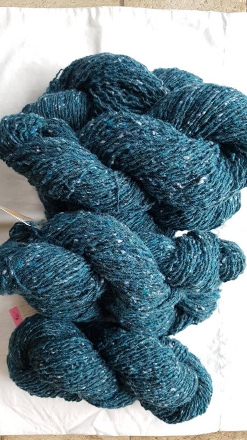 Pode incluir: Fio azul-petr&oacute;leo com manchas brancas, torcido em forma de bola.