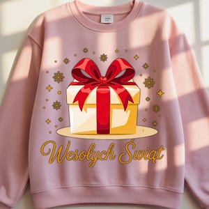 May include: A light pink sweatshirt featuring a graphic of a gift box with a red bow. The gift box is yellow and white, with decorative snowflakes and stars. The text "Wesołych Świąt" is written in gold script.