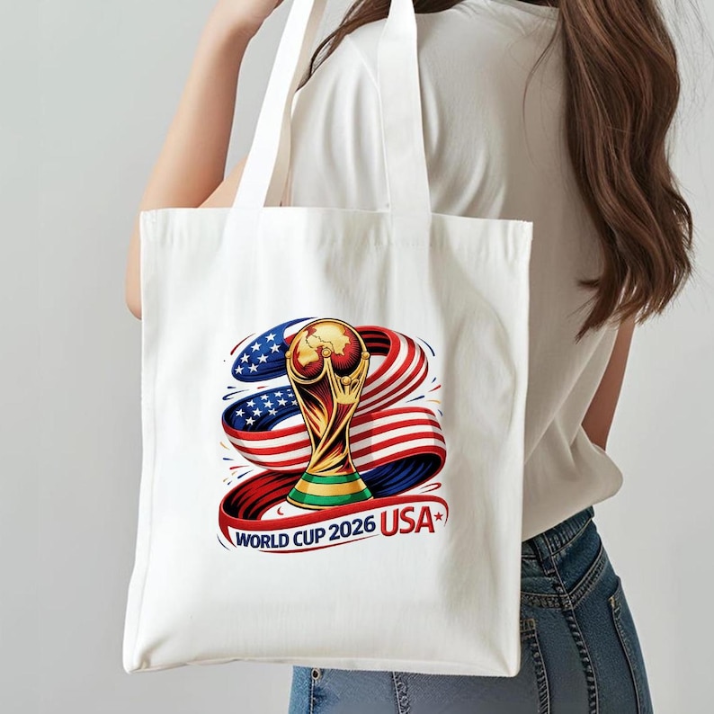 May include: White tote bag featuring a colorful graphic of the World Cup trophy, with red, white, and blue ribbons and the text "WORLD CUP 2026 USA". The design incorporates stars and stripes, celebrating the event.