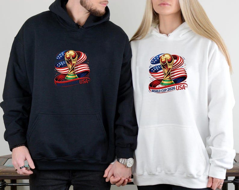 May include: Navy blue and white hooded sweatshirts featuring a graphic of a gold trophy, the American flag, and the text "USA". The sweatshirts have a front pocket and a drawstring hood. The design is centered on the front of the sweatshirts.