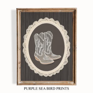 May include: Framed print featuring a pair of white cowboy boots on a dark brown background, inside a cream-colored oval with a lace-like border. The frame is a light brown color. The text "PURPLE SEA BIRD PRINTS" is at the bottom.
