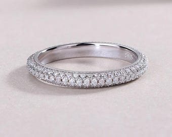 May include: A silver ring featuring two rows of small, clear gemstones encircling the band. The ring is presented on a pale pink surface, highlighting its polished, reflective finish. A classic design, suitable for various occasions.