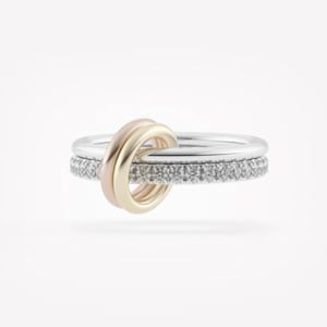 May include: Three rings against a white background. The top ring is gold, the middle ring is silver, and the bottom ring is silver with small, clear stones. The gold ring is interlocked with the silver rings.