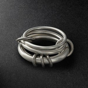 May include: A sterling silver ring composed of multiple interlocking circular bands of varying thicknesses. The metal has a polished, reflective finish, and the inner band features a small, stamped 925 hallmark indicating silver purity.