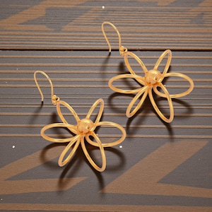May include: A pair of gold-colored flower earrings. Each earring features a floral design with six curved petals radiating from a central sphere. The earrings have a hook closure.