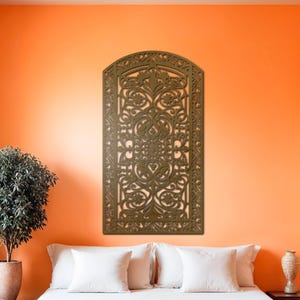 May include: A bedroom with an orange wall and a large, ornate, brown wooden wall panel. The bed has white linens and an orange throw. A small tree in a pot and a vase are also in the room.