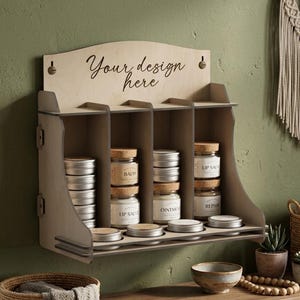May include: A light-coloured wooden wall-mounted display shelf with four vertical compartments. The top panel features the text "Your design here". The shelf holds stacks of small round metal tins and glass jars with cork lids labelled "Balm", "Lip Salve", and "Ointment".