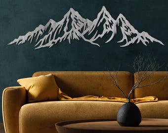 May include: A silver metal mountain range wall art piece. The artwork features a detailed depiction of a mountain range with peaks and valleys. The piece is mounted on a dark teal wall above a mustard-colored sofa with a yellow pillow.
