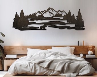 May include: A dark brown wooden wall art piece depicting a mountain range, trees, and a bear. The artwork is mounted above a bed with white bedding and a wooden headboard. The piece is a decorative element for a bedroom.