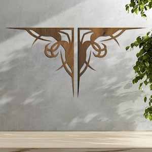 May include: Two-piece wooden wall decor with an intricate, symmetrical design. The pieces are a warm brown color and feature a series of curved lines and pointed edges. The decor is mounted on a light gray wall, with a wooden surface below.