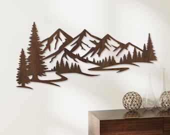 May include: A brown wooden wall art piece depicting a mountain range with trees and a river. The artwork is cut out of wood, creating a silhouette effect. The piece is mounted on a white wall.