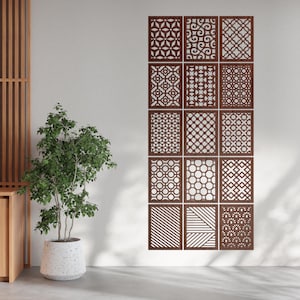 Può includere: Un set di dodici pannelli decorativi marroni con vari disegni geometrici e floreali ritagliati. I pannelli rettangolari sono montati su una parete bianca. Una pianta in vaso è in primo piano. I pannelli misurano circa 60 cm x 40 cm.