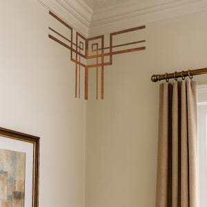 May include: Decorative copper-colored wall art in a corner, featuring a geometric design. The art is installed on a cream-colored wall, with a white ceiling and a brown curtain visible in the background. The art adds a touch of elegance to the room.
