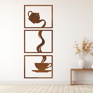 Könnte beinhalten: Dreiteilige Wandkunst aus Holz mit Kaffee- oder Teemotiv. Das obere Feld zeigt eine Teekanne beim Ausgießen, das mittlere Feld den Strom und das untere Feld eine Tasse und Untertasse. Die Kunst ist braun und an einer weißen Wand befestigt.