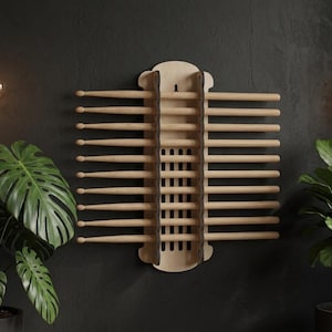 May include: A wall-mounted wooden drumstick rack featuring a light-colored central panel with a vertical grid design and two dark side supports. The rack holds ten pairs of light-colored wooden drumsticks arranged horizontally in parallel rows.