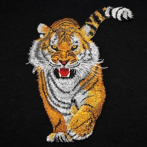 May include: Embroidered tiger patch with orange, black, white, and yellow thread on a black background. The tiger is depicted in a dynamic, aggressive pose with its mouth open, showcasing its teeth. The patch is likely for clothing or accessories.