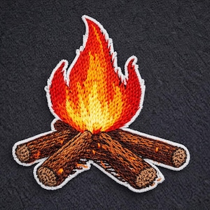 May include: Embroidered patch of a campfire. The flames are red, orange, and yellow, with a white outline. The logs are brown with a textured look, also outlined in white. The patch is on a dark grey fabric.