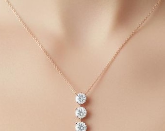 May include: A delicate rose gold necklace featuring three round, sparkling gemstones. The pendant hangs vertically, showcasing the brilliant cut of the stones. The necklace is displayed against a neutral background.