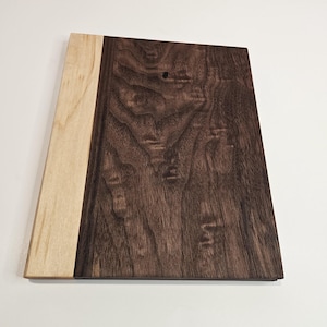 May include: A rectangular wooden cutting board with a light-colored wood section on the left and a dark brown wood section on the right. The wood grain is visible, and the board is set against a white background.