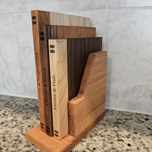 May include: A wooden cutting board set with a holder. The set includes four rectangular boards of varying wood tones, labeled "Fruit & Vegetables", "Cheese & Bread", and "Meats & Fish". The holder is made of light brown wood.
