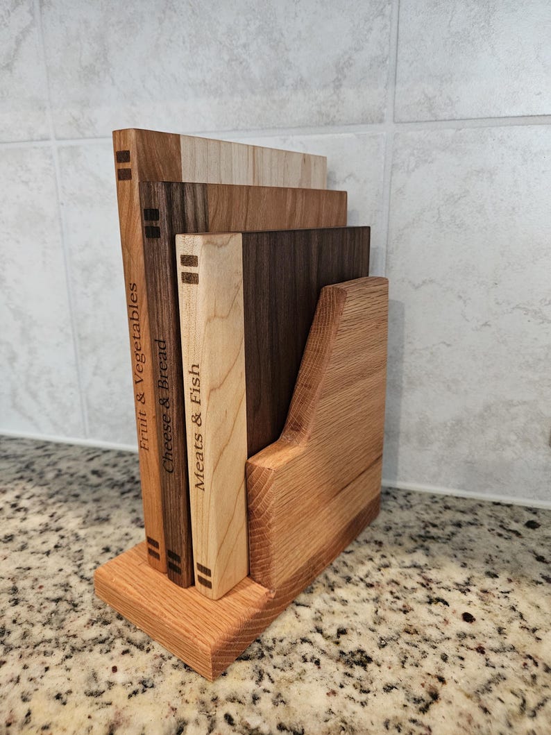 May include: A wooden cutting board set with a holder. The set includes four rectangular boards of varying wood tones, labeled "Fruit & Vegetables", "Cheese & Bread", and "Meats & Fish". The holder is made of light brown wood.