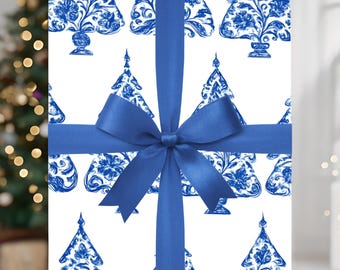 Puede incluir: Un regalo envuelto con un fondo blanco con un patrón de árboles de Navidad florales azules. El regalo está atado con una cinta y un lazo de satén azul. Un árbol de Navidad borroso es visible en el fondo.