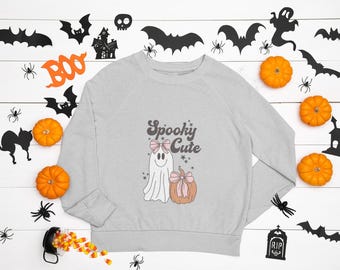 Może przedstawiać: Jasnoszara bluza z motywem Halloween. Projekt przedstawia ducha z różową kokardą, dynię z różową kokardą i napis "Spooky Cute". Tło zawiera pomarańczowe dynie, nietoperze, pająki i nawiedzony dom.